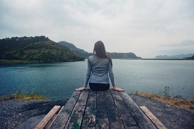 A girl sitting on a picnic table with her back turned looking at the water