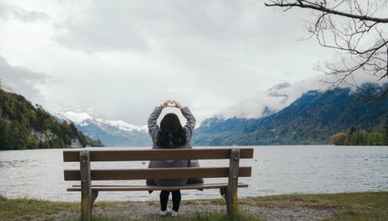 Girl on a bench with her back turned looking out at the mountains and making a heart with her hands
