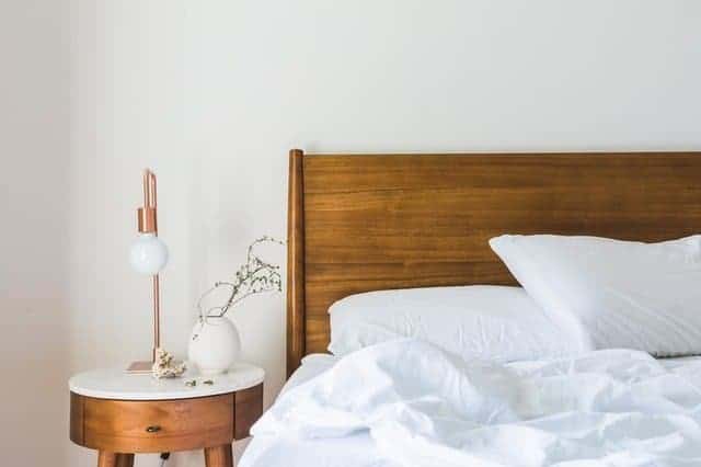 A bed with white sheets and a wooden headboard next to a matching nightstand