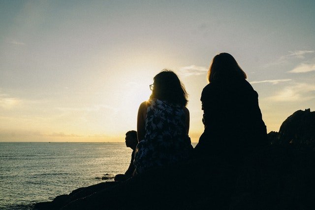 A silhouette of two women facing a body of water