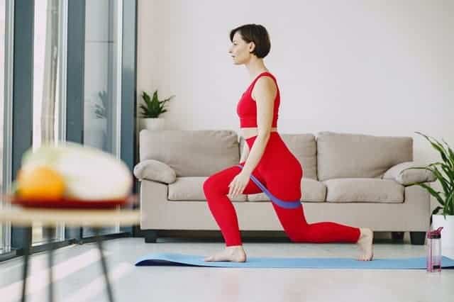 A woman in athletic gear in her living room doing a yoga pose with a resistance band