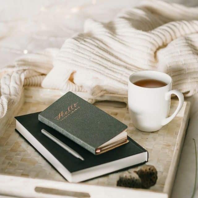 Two notebooks and a coffee mug on a bed next to a blanket