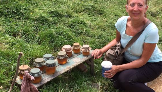 A woman holding a coffee smiling at the camera next to jars of honey