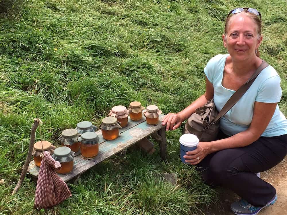 A woman holding a coffee smiling at the camera next to jars of honey