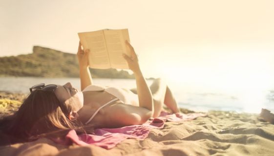 Woman laying at the beach reading a book