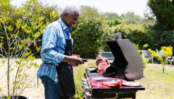 An older man standing in front of a grill putting a steak on it