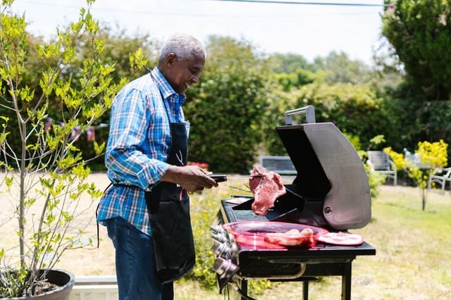 An older man standing in front of a grill putting a steak on it