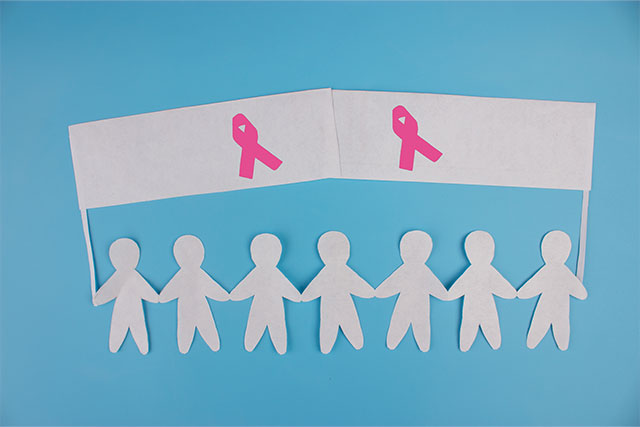 Paper cut outs of people holding a sign with Breast Cancer pink ribbons